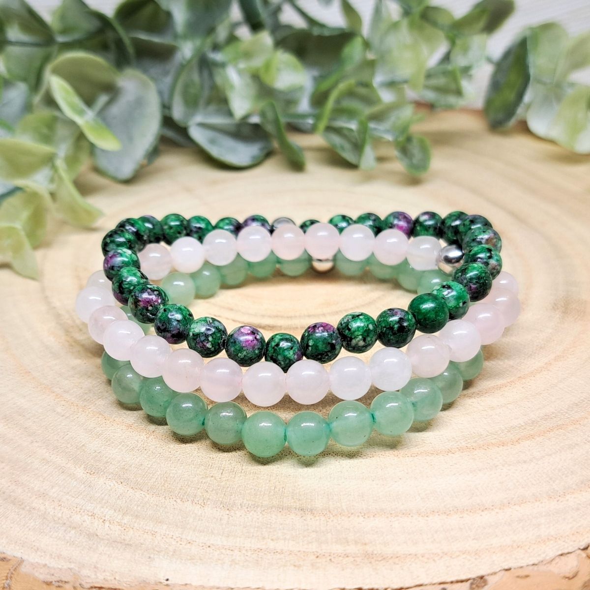 3 green and pink crystal bead bracelets on a wood surface.